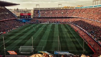 Packendes Fußballspiel in einem vollbesetzten Stadion mit einer lebendigen Zuschauermenge und einem breiten Blick auf das Spielfeld während der goldenen Stunde.