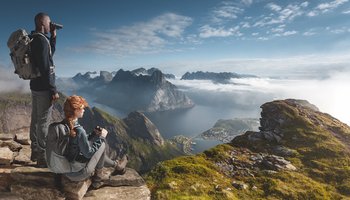 Das Foto zeigt einen Mann und eine Frau, die durch ein Fernglas eine schöne Berglandschaft beobachten.
