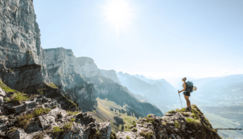 Das Foto zeigt eine Sportlerin auf einem Berg stehend bei Sonne und schöner Aussicht.