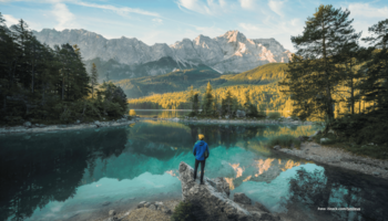 Das Foto zeigt eine Person vor dem schönen, blauen Eibsee in Bayern stehend bei Sonnenschein.