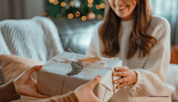 Das Foto zeigt eine Frau, die vor dem Weihnachtsbau ein Geschenk überreicht bekommt.