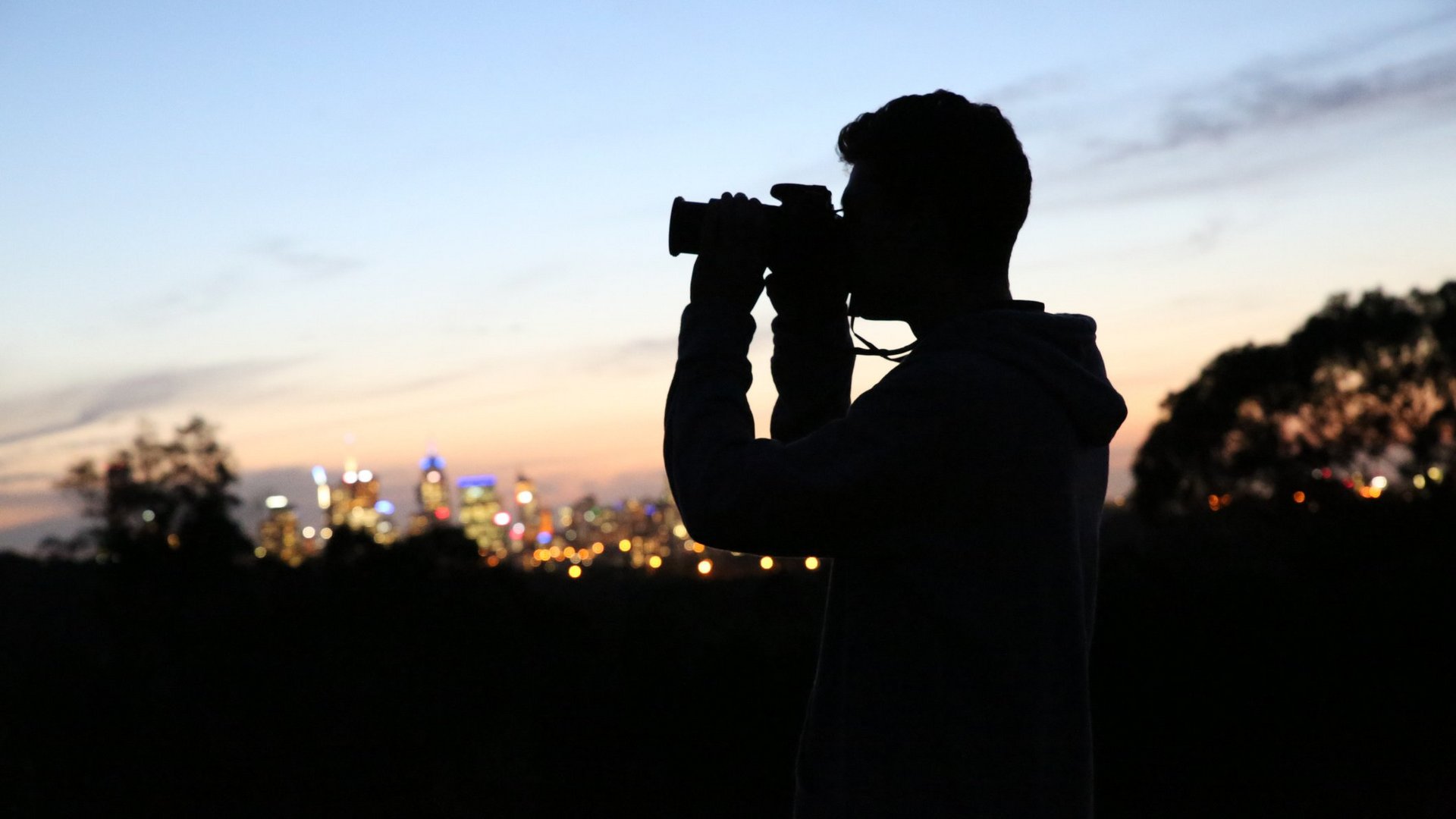 Das Foto zeigt die Silhouette eines Mannes, der den Sonnenuntergang mit einer Kamera fotografiert.