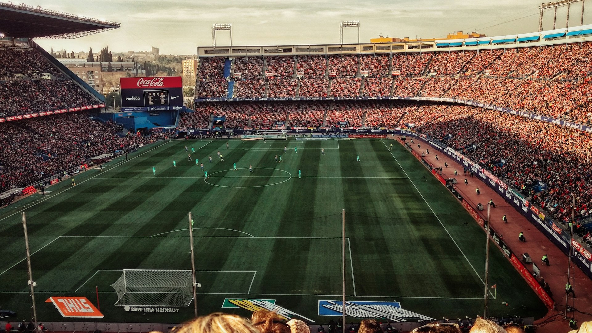 Packendes Fußballspiel in einem vollbesetzten Stadion mit einer lebendigen Zuschauermenge und einem breiten Blick auf das Spielfeld während der goldenen Stunde.