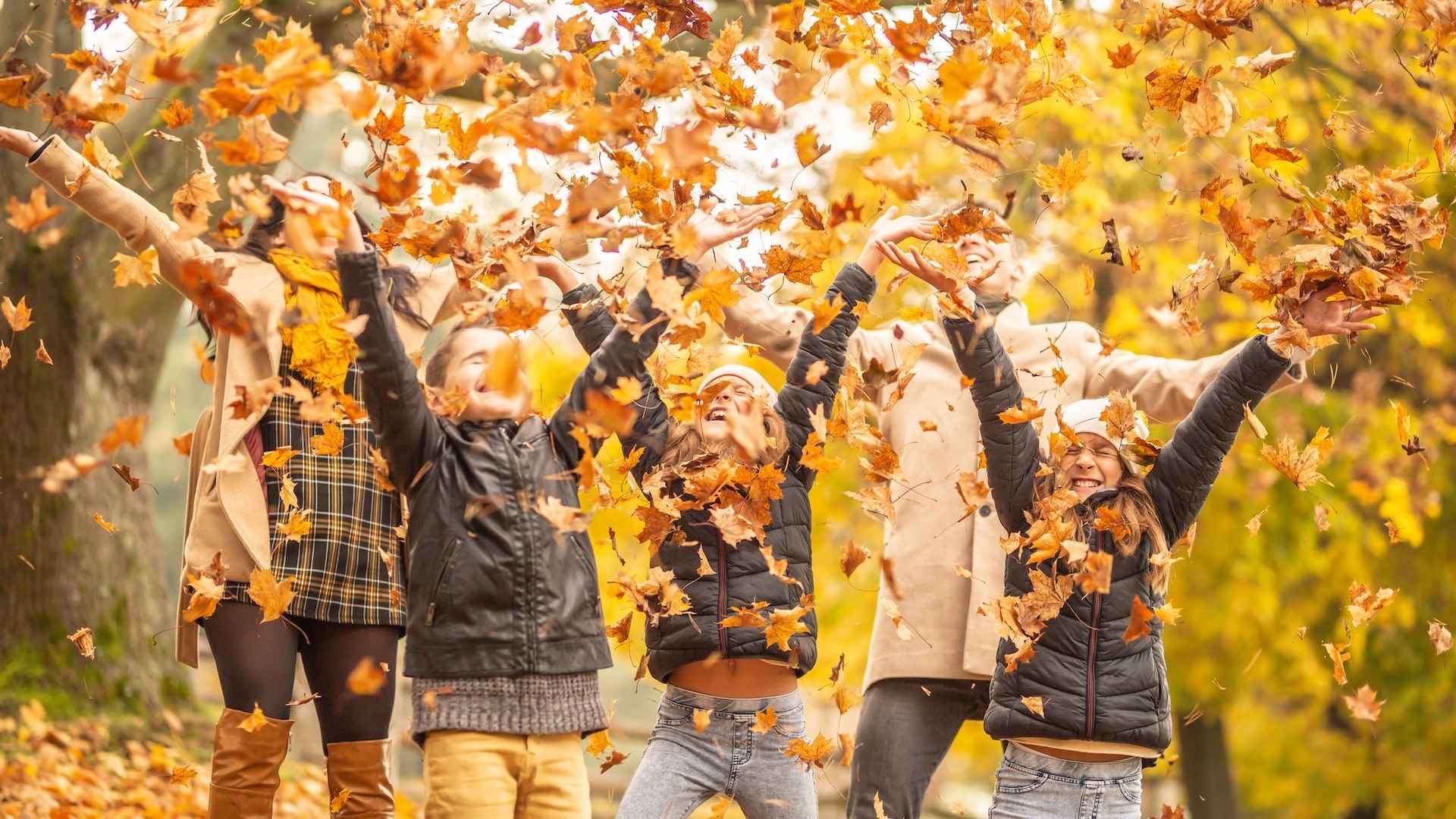 Familie wirft im Herbst gefallene Blätter durch die Luft